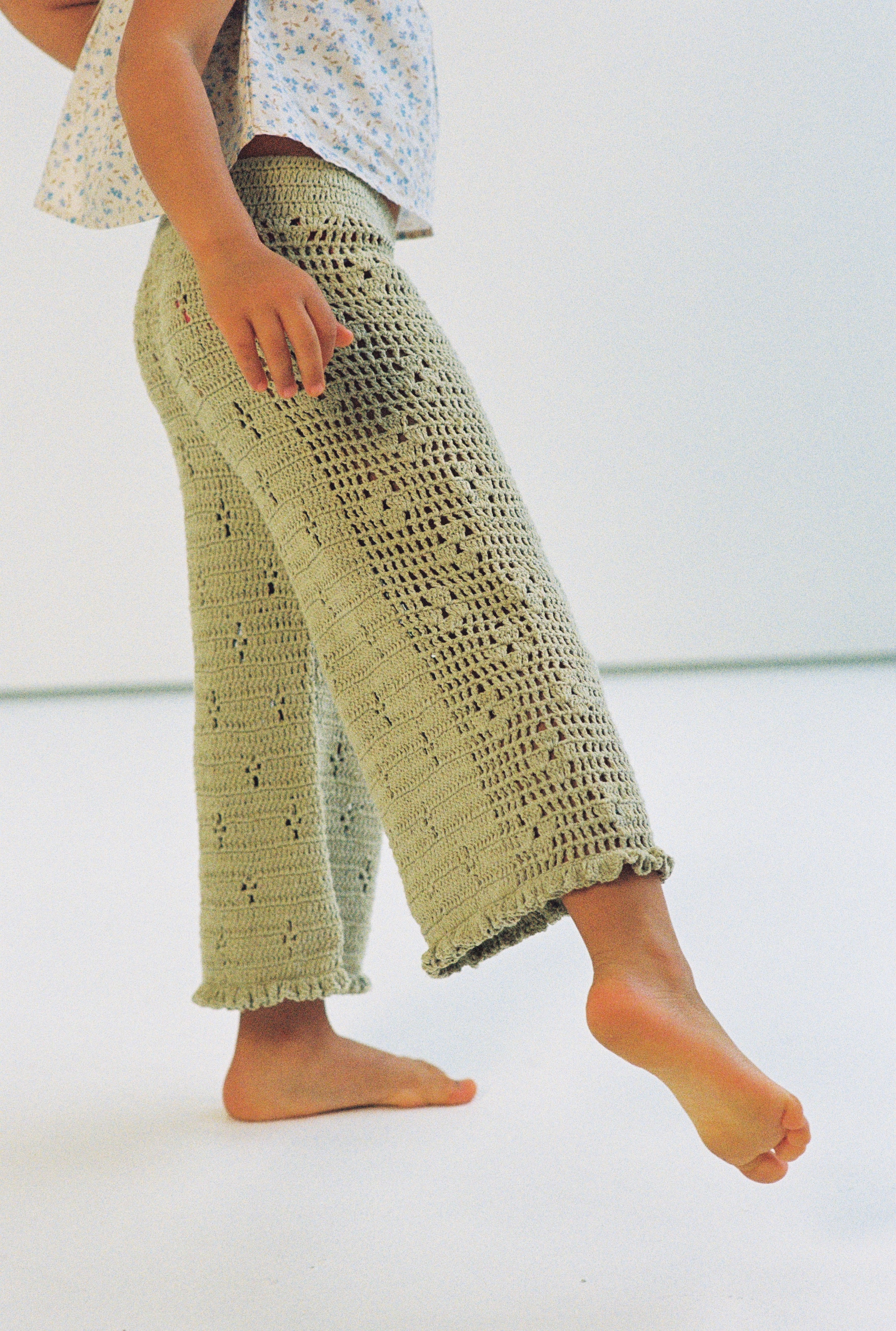 girl wears 100% cotton crochet pants in moss colour with floral filet design and elasticated waist with one shoulder floral print top in 100% cotton