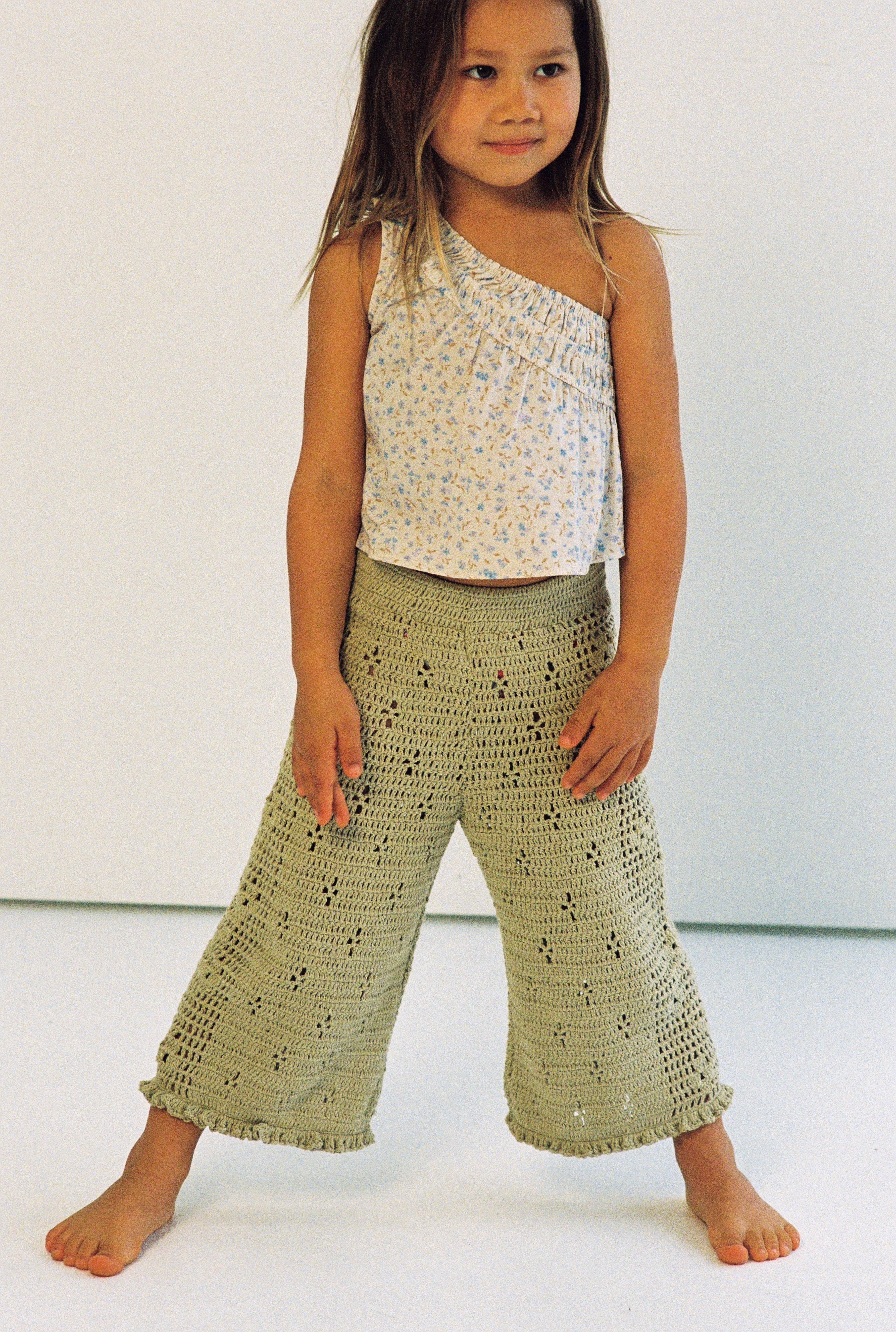 girl wears 100% cotton crochet pants in moss colour with floral filet design and elasticated waist with one shoulder floral print top in 100% cotton
