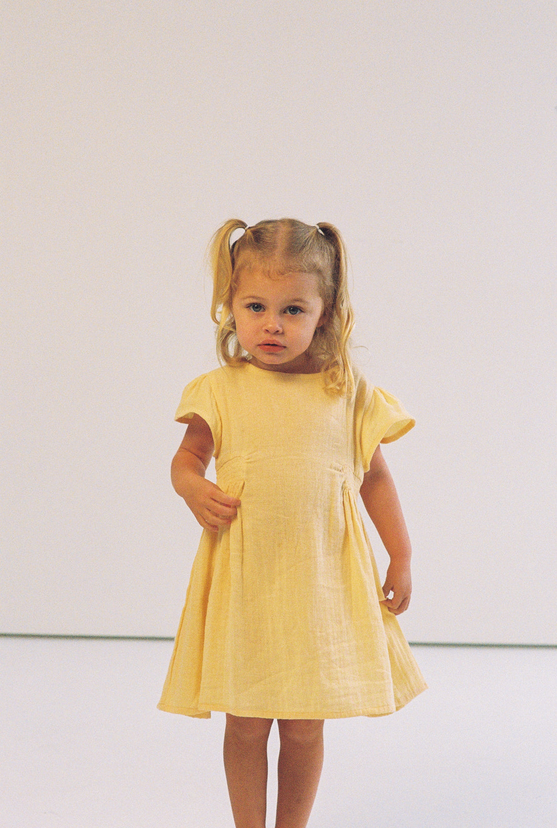 toddler girl wearing 100% cotton dress with shirring and flutter sleeves in butter yellow