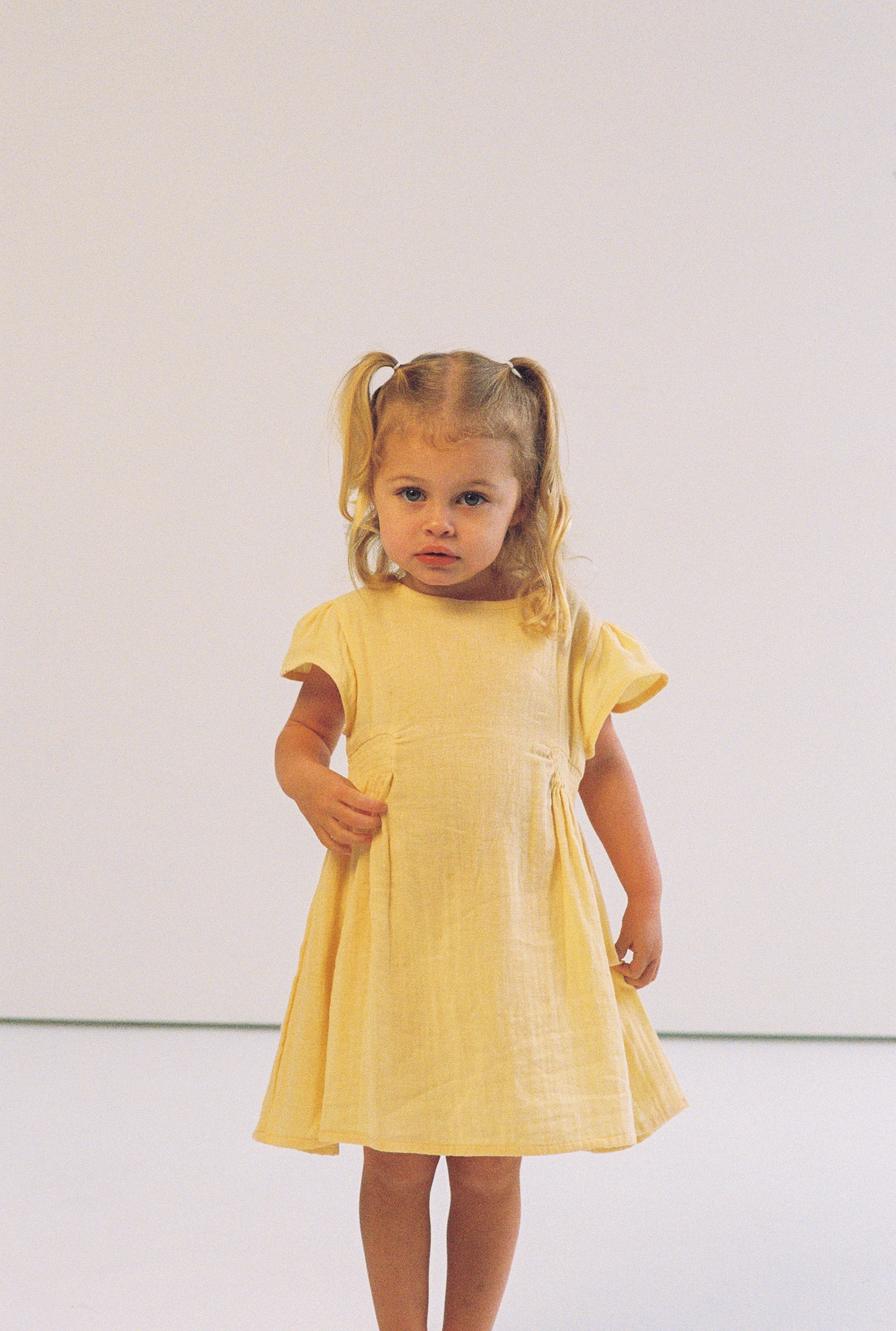 toddler girl wearing 100% cotton dress with shirring and flutter sleeves in butter yellow