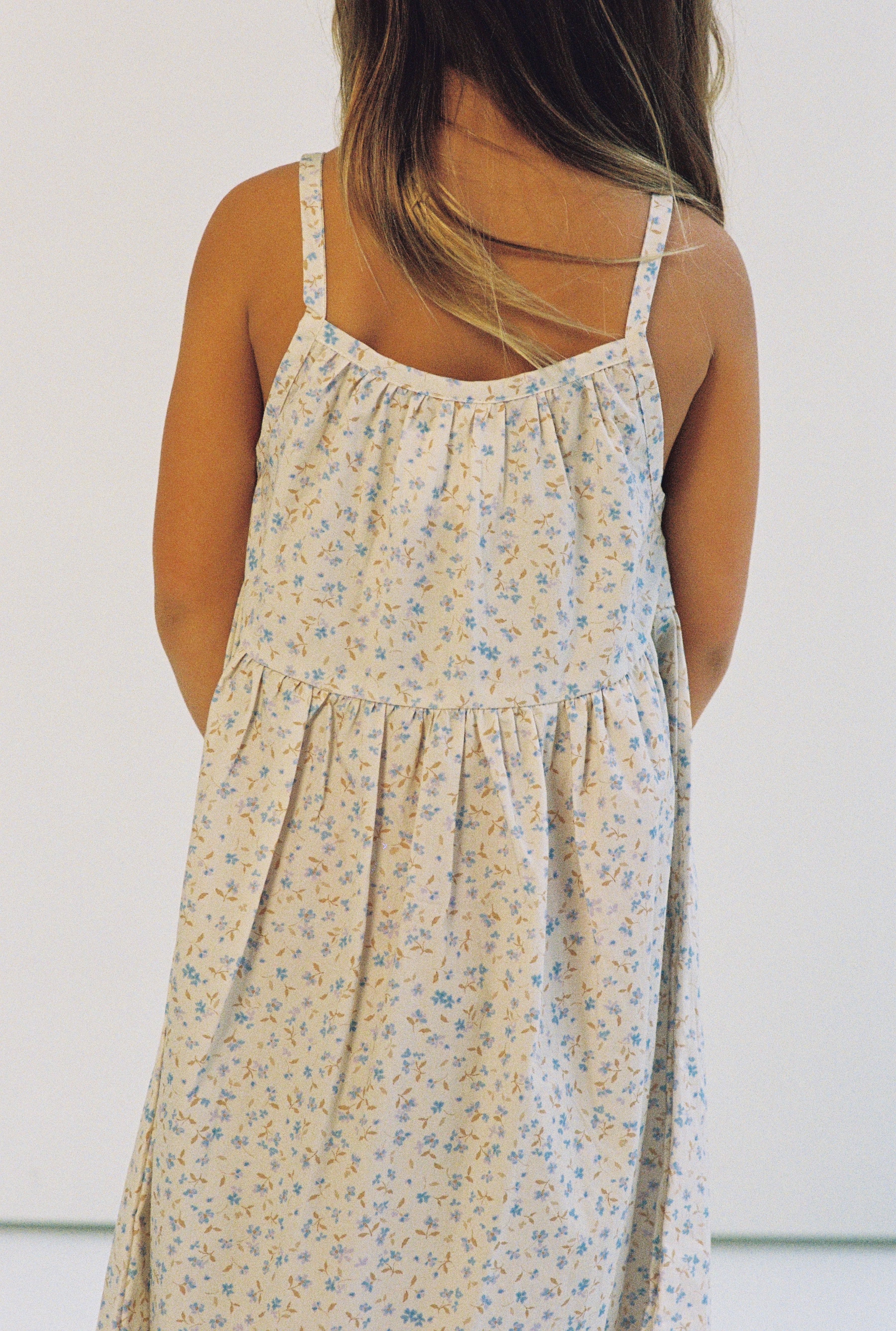 girl wearing 3/4 length floral printed dress made from 100% cotton poplin with thin straps and gathers at the chest and waist