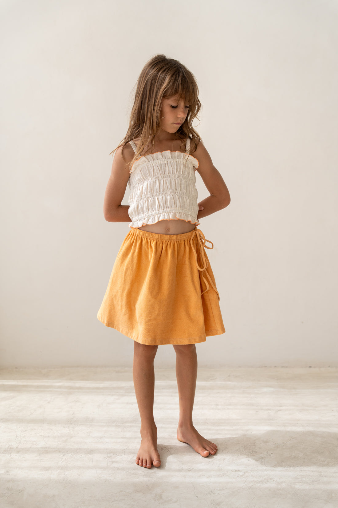 girl wearing ecru cotton shirred crop and orange cotton terry skirt by Illoura the label