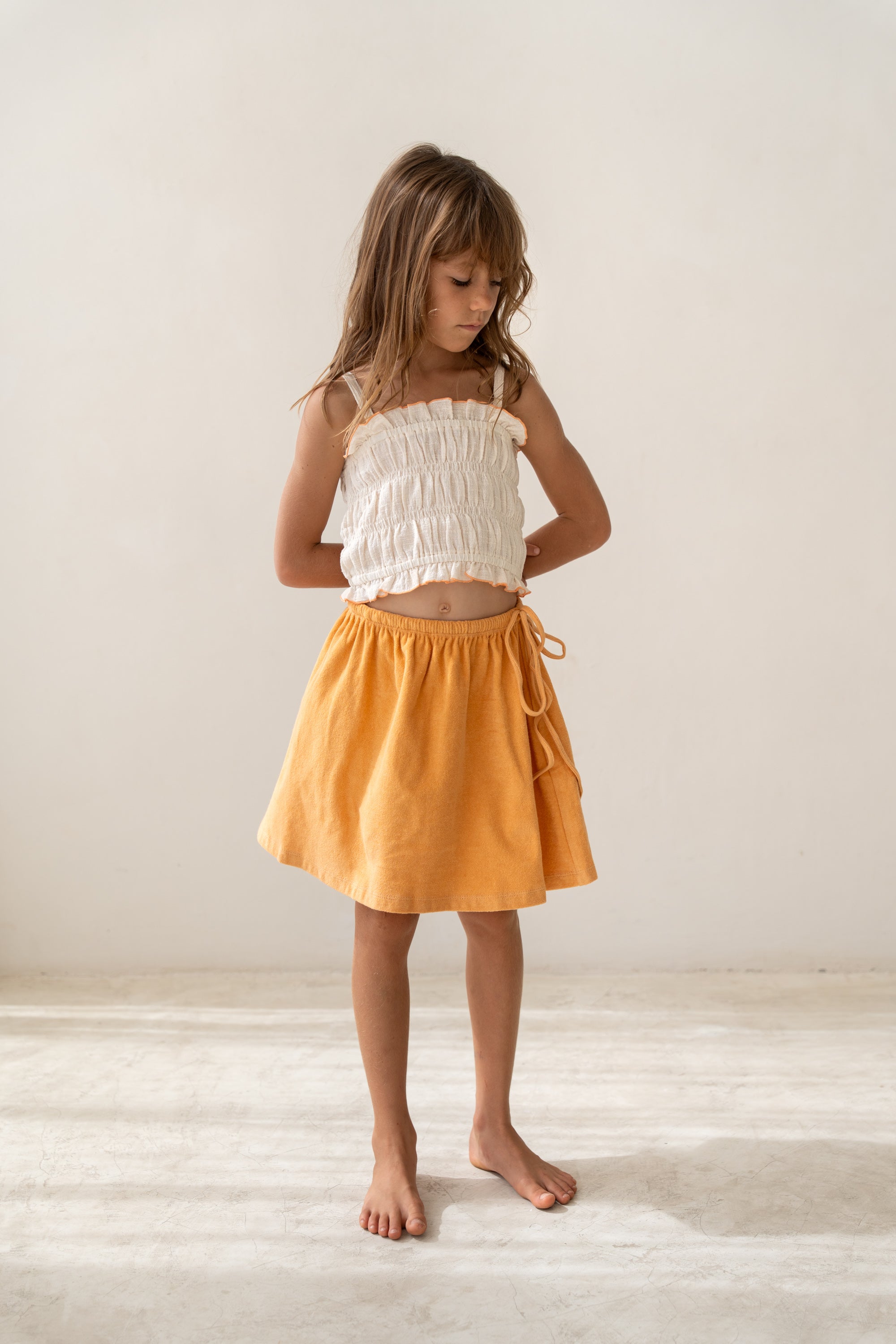 girl wearing ecru cotton shirred crop and orange cotton terry skirt by Illoura the label