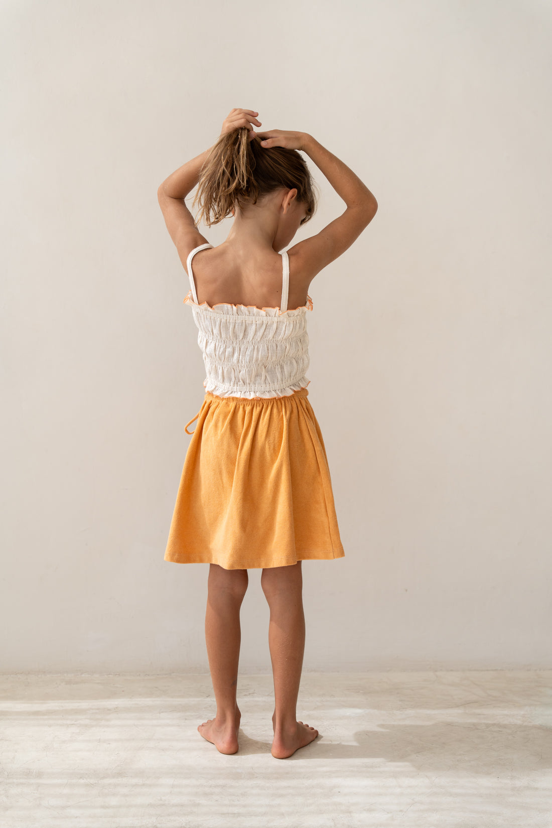 girl wearing ecru cotton shirred crop and orange cotton terry skirt by Illoura the label
