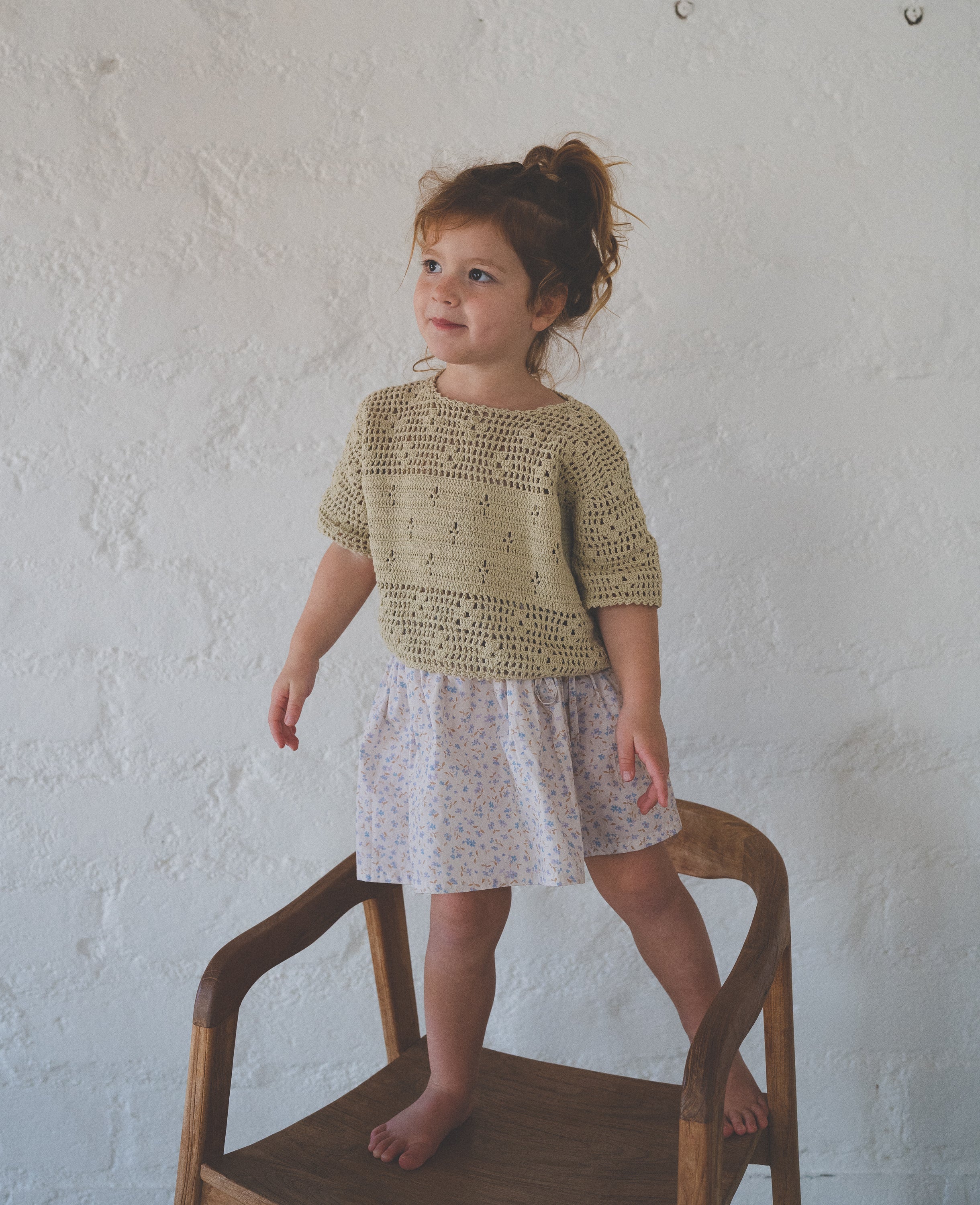 girl wears 100% cotton t-shirt style crochet top in moss green colour featuring floral filet design and 100% cotton poplin skirt in blue floral print