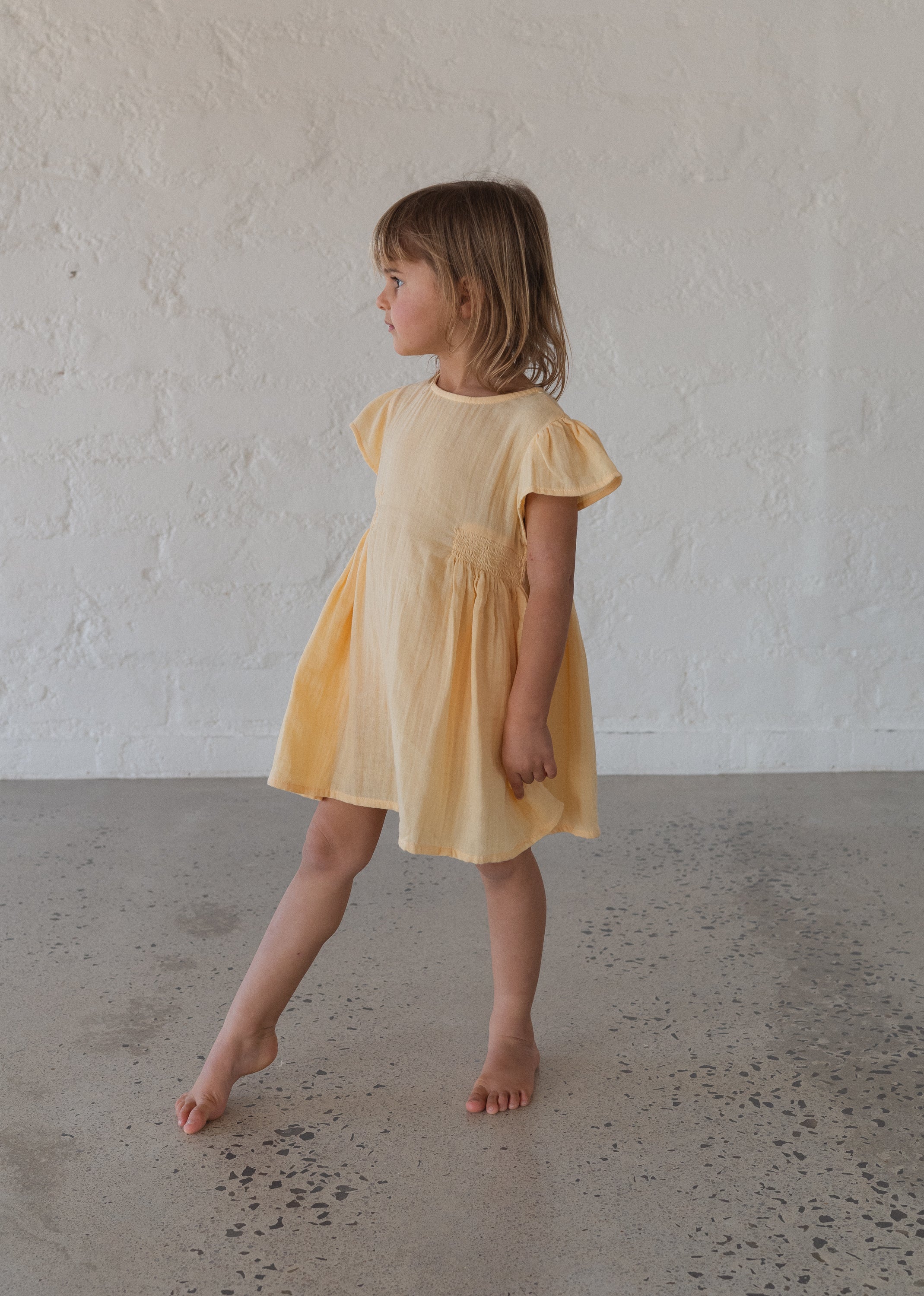 toddler girl wearing 100% cotton dress with shirring and flutter sleeves in butter yellow
