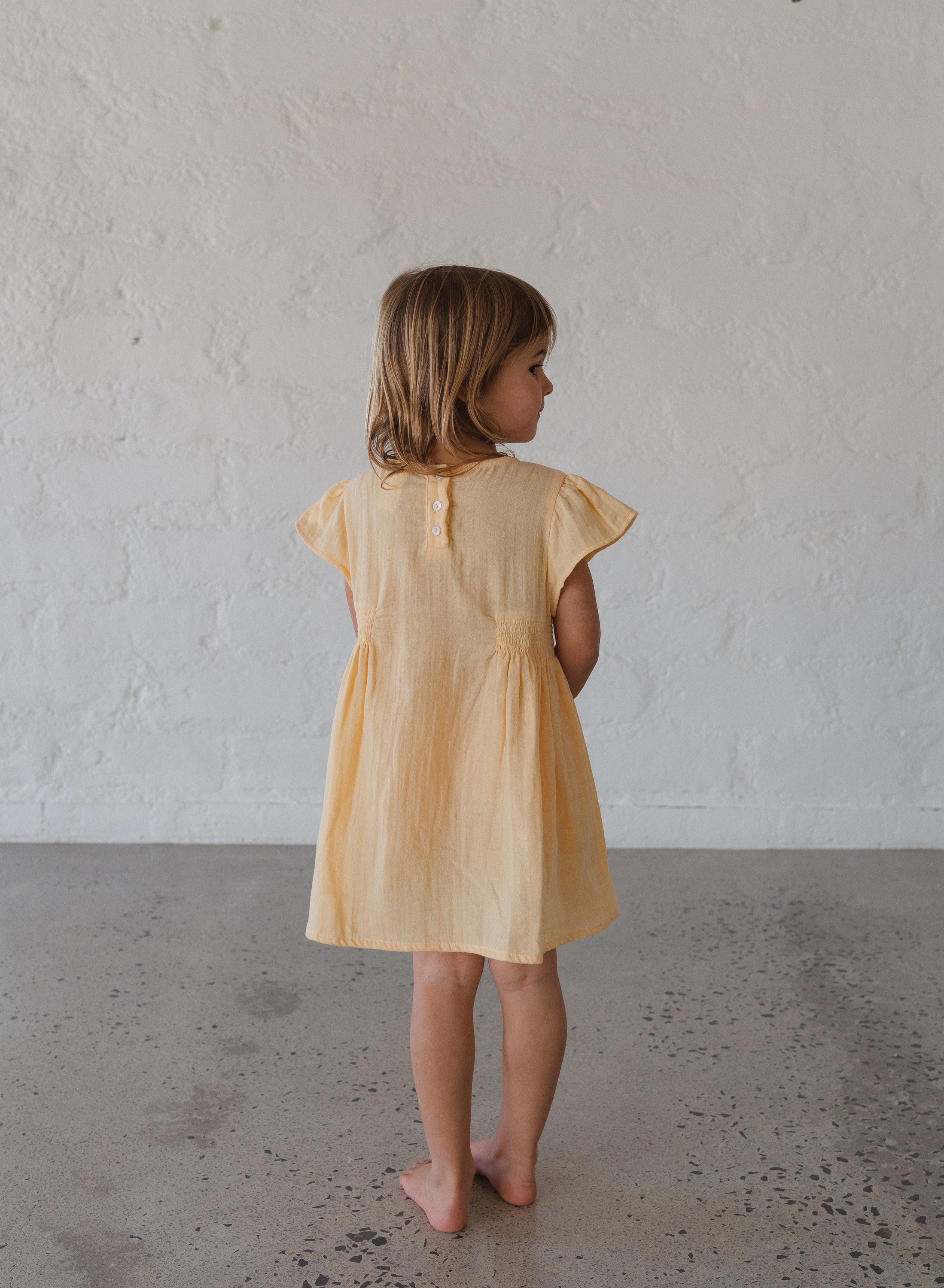 toddler girl wearing 100% cotton dress with shirring and flutter sleeves in butter yellow