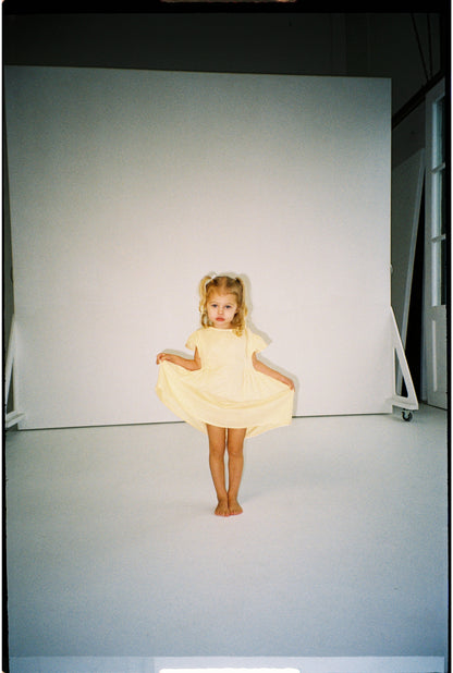 toddler girl wearing 100% cotton dress with shirring and flutter sleeves in butter yellow