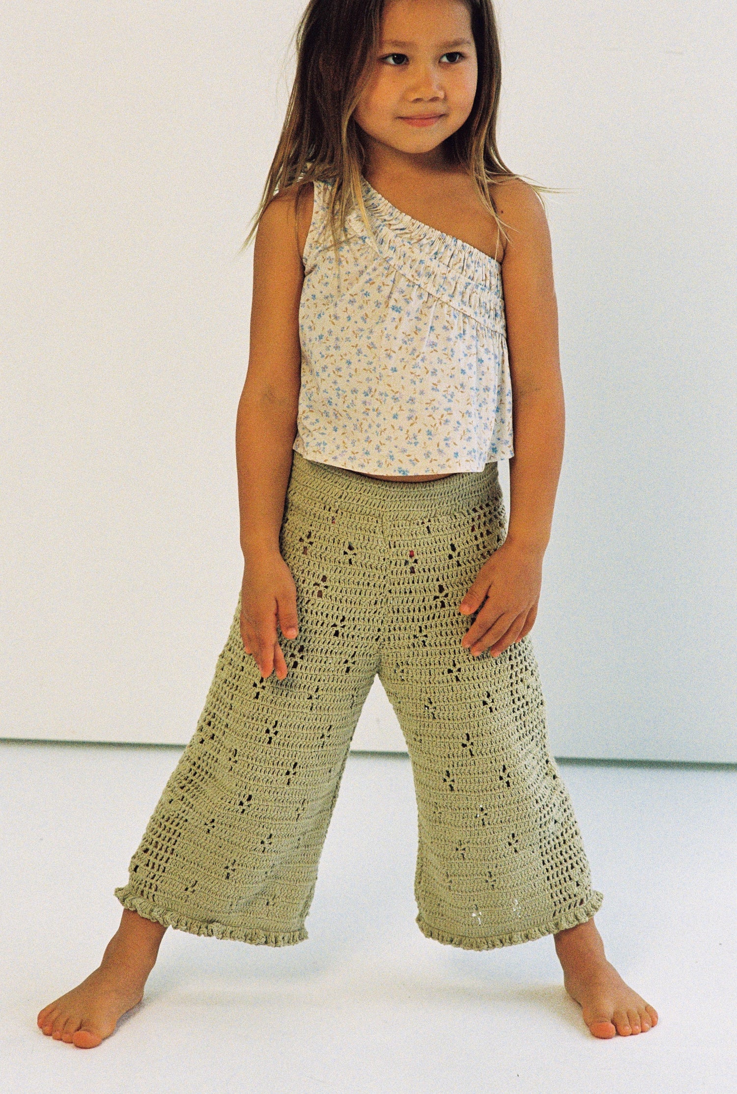 girl wears 100% cotton crochet pants in moss colour with floral filet design and elasticated waist with one shoulder floral print top in 100% cotton