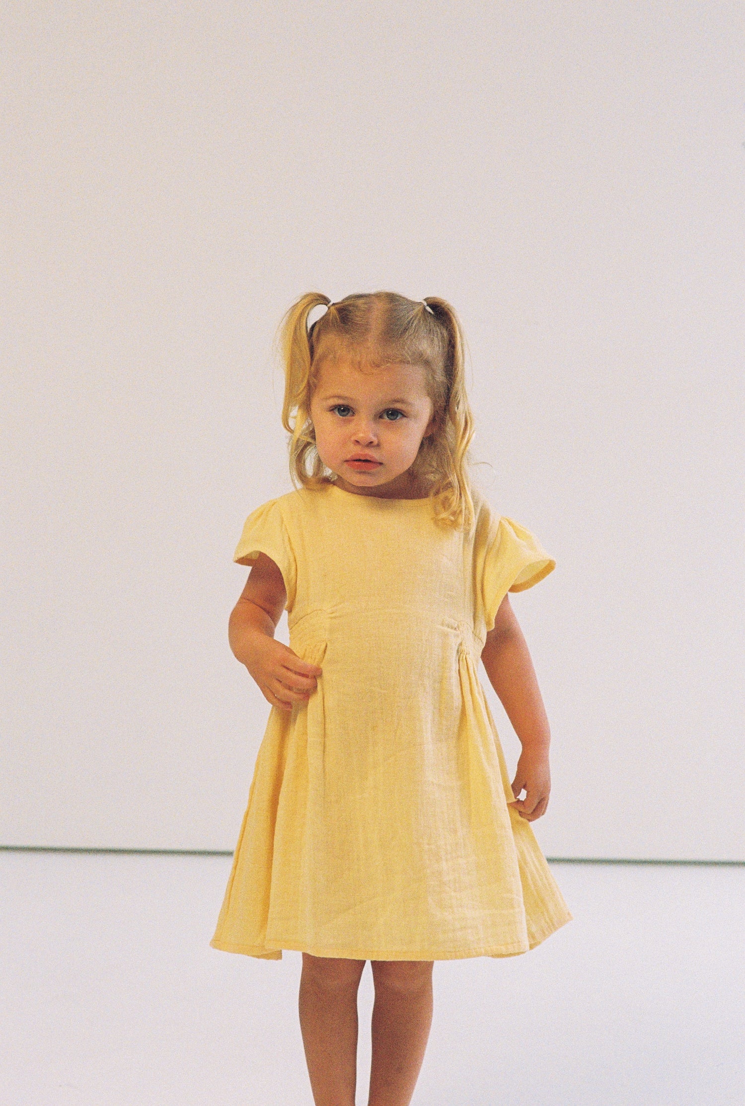 toddler girl wearing 100% cotton dress with shirring and flutter sleeves in butter yellow