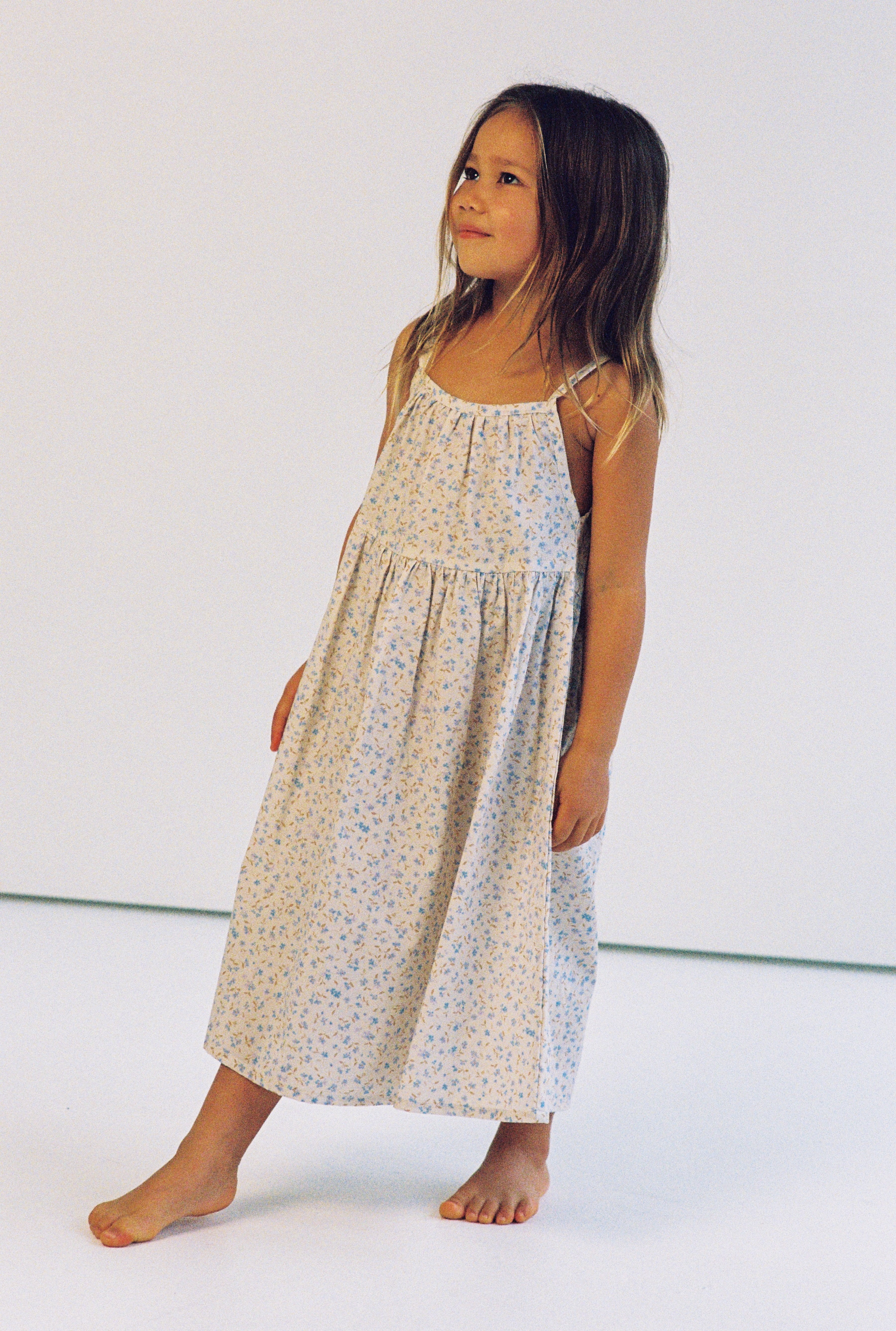 girl wearing 3/4 length floral printed dress made from 100% cotton poplin with thin straps and gathers at the chest and waist