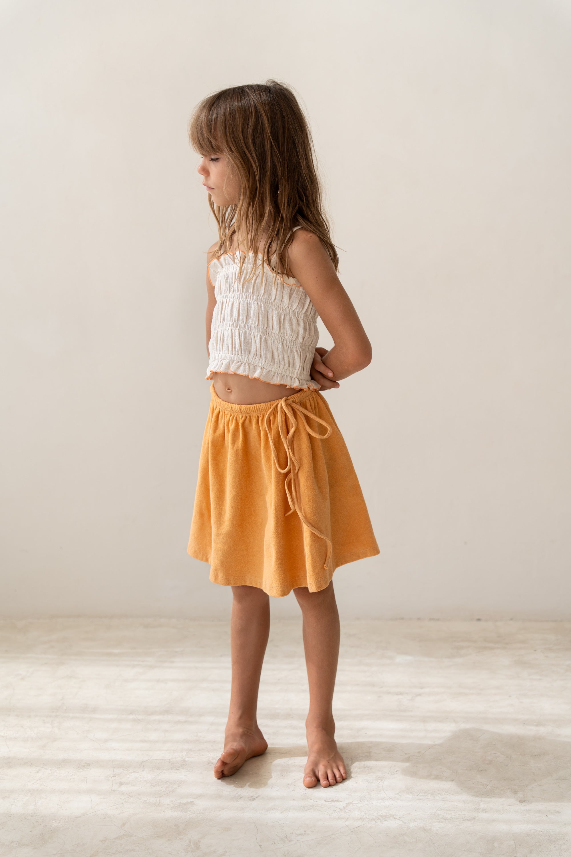 girl wearing ecru cotton shirred crop and orange cotton terry skirt by Illoura the label