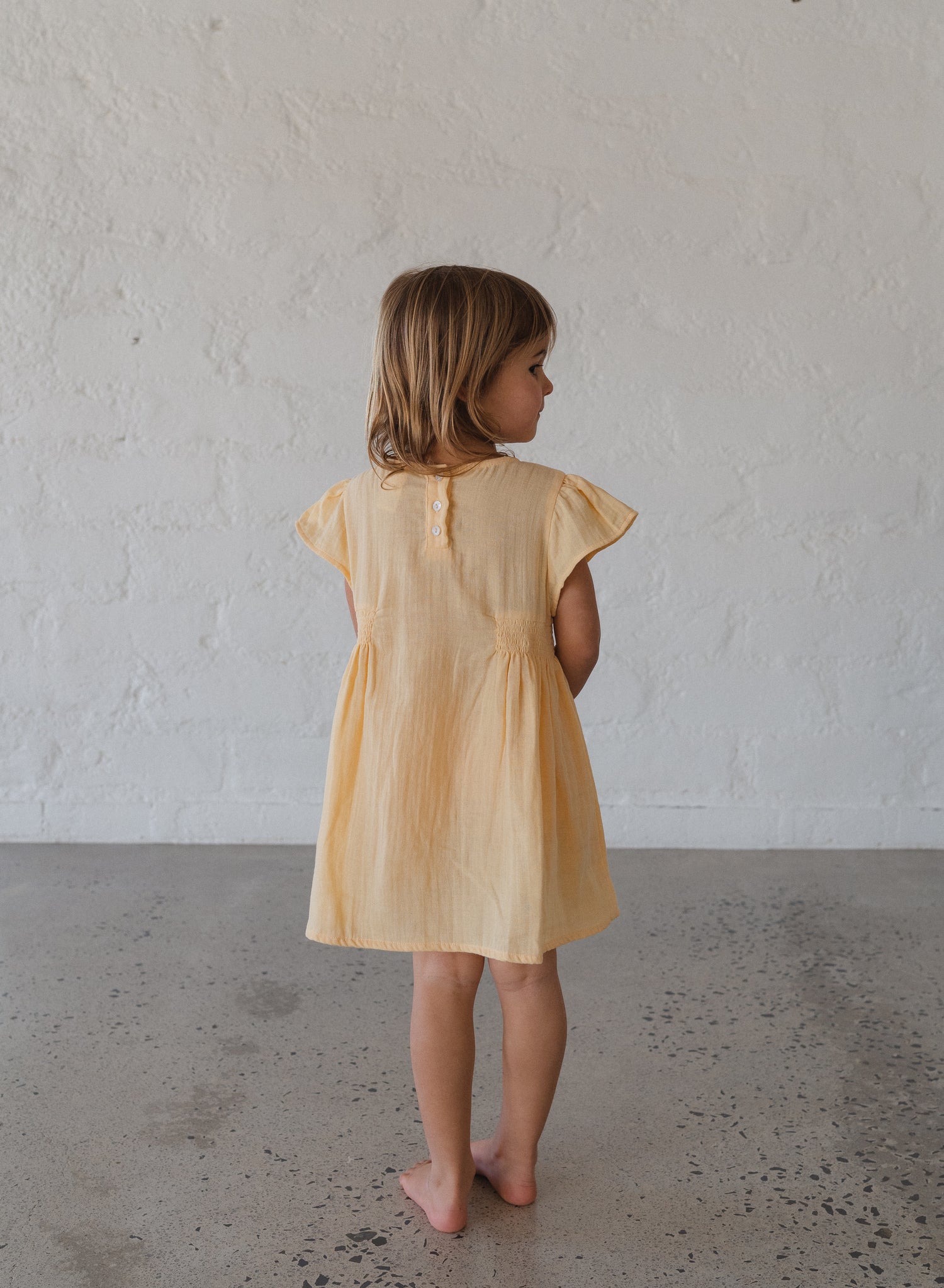 toddler girl wearing 100% cotton dress with shirring and flutter sleeves in butter yellow
